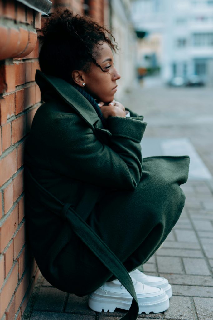A woman sitting against a brick wall, looking away with a pensive expression — representing a client feeling stuck in therapy despite meaningful progress.